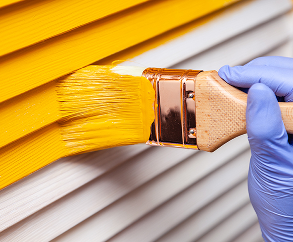 a person wearing a blue glove painting an exterior yellow with a paint brush