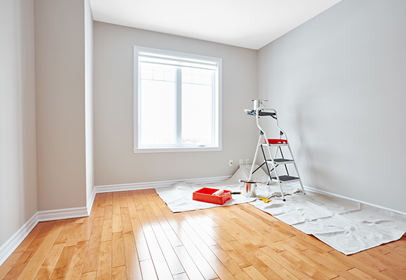an empty room with a step ladder, painting items and rags laid out over the corner of the room's laminate floor