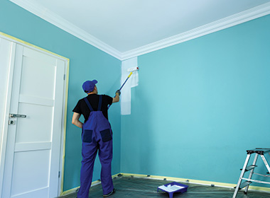 a man painting a room blue with plastic over the carpet to protect it